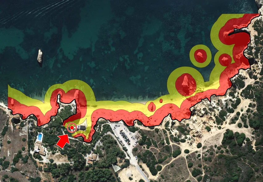 Uma imagem aérea de uma costa com sobreposições coloridas que indicam diferentes zonas ou níveis, com um símbolo de seta vermelha apontando para uma área específica e círculos destacados em algumas zonas.