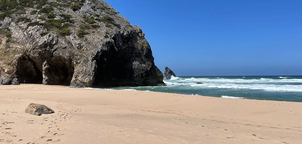 Visão de uma praia tranquila com cavernas nas falésias e ondas suaves no oceano.